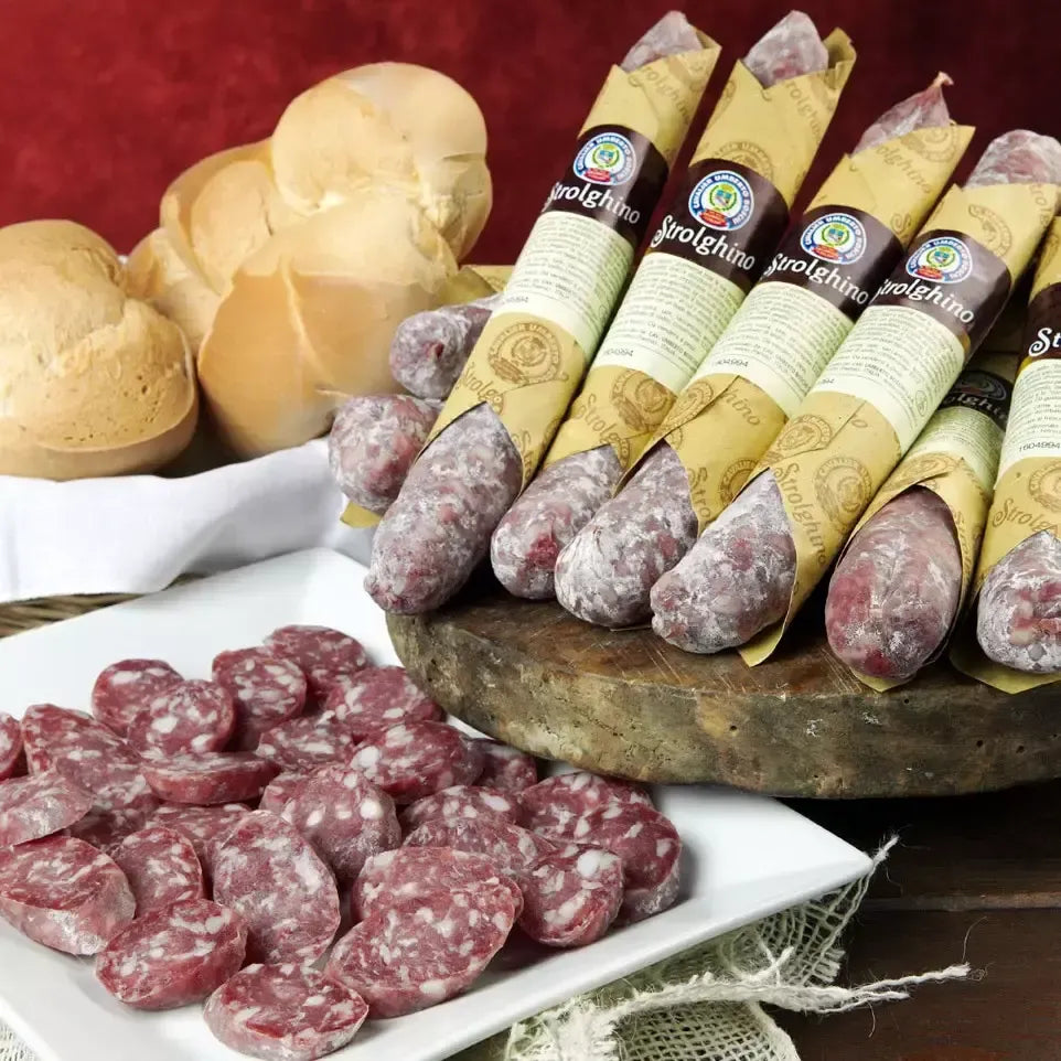 En velsmakende strolghino ligger på et autentisk rustikt skjærebrett, omgitt av nybakte brød. På et hvitt fat ved siden av inviterer salamiskiver til å ta en bit.