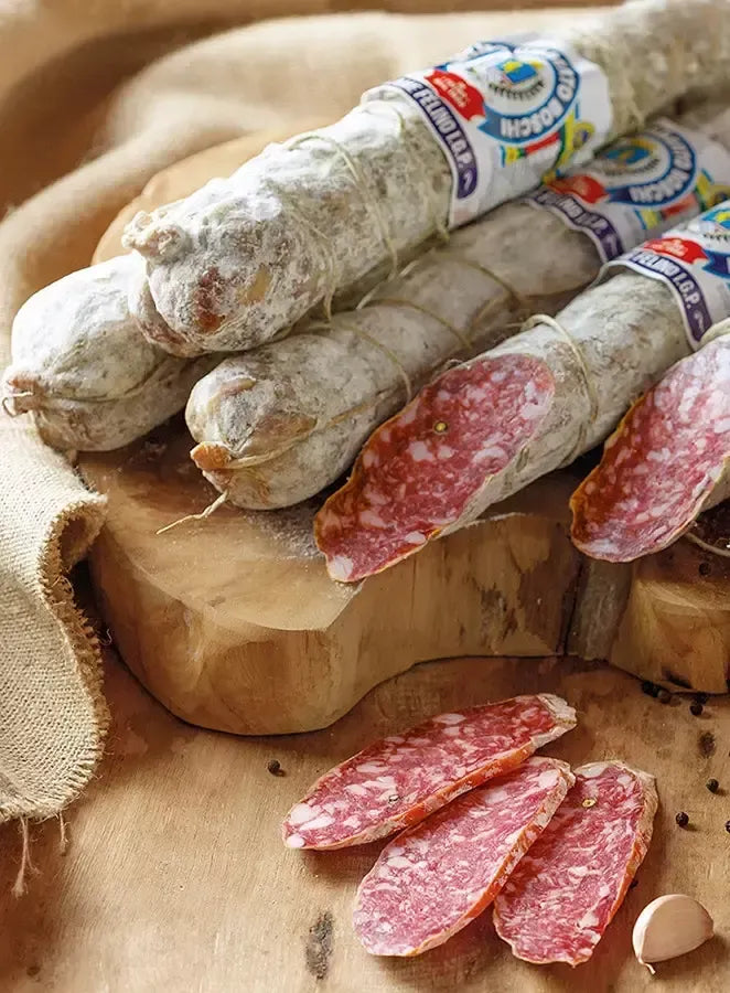 Ein Gourmet-Erlebnis mit der Salami aus Felino IGP, aufgeschnitten und serviert auf einem rustikalen Schneidebrett, das das würzige Aroma der italienischen Tradition hervorruft.