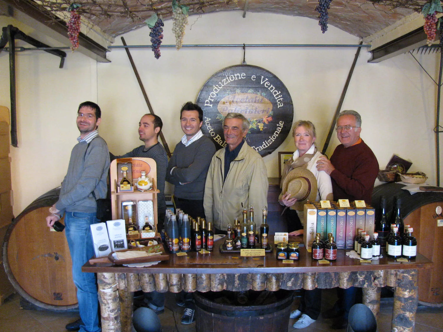 Gruppo sorridente in una cantina accogliente tra bottiglie di vini locali, pronto per una degustazione indimenticabile.