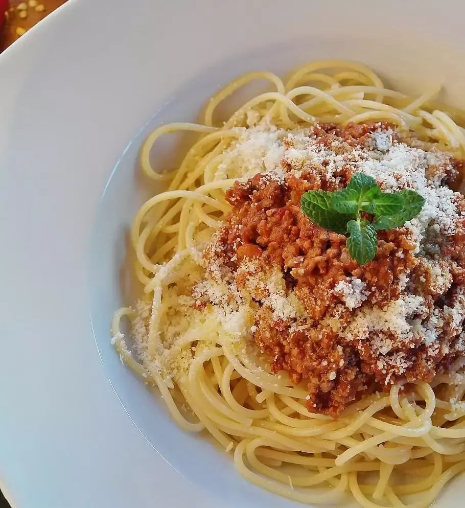 Un plato de tagliatelle, cubiertos con una cremosa salsa de carne piamontesa, enriquecida con queso parmesano y una hoja de albahaca, sobre un fondo rústico clásico.