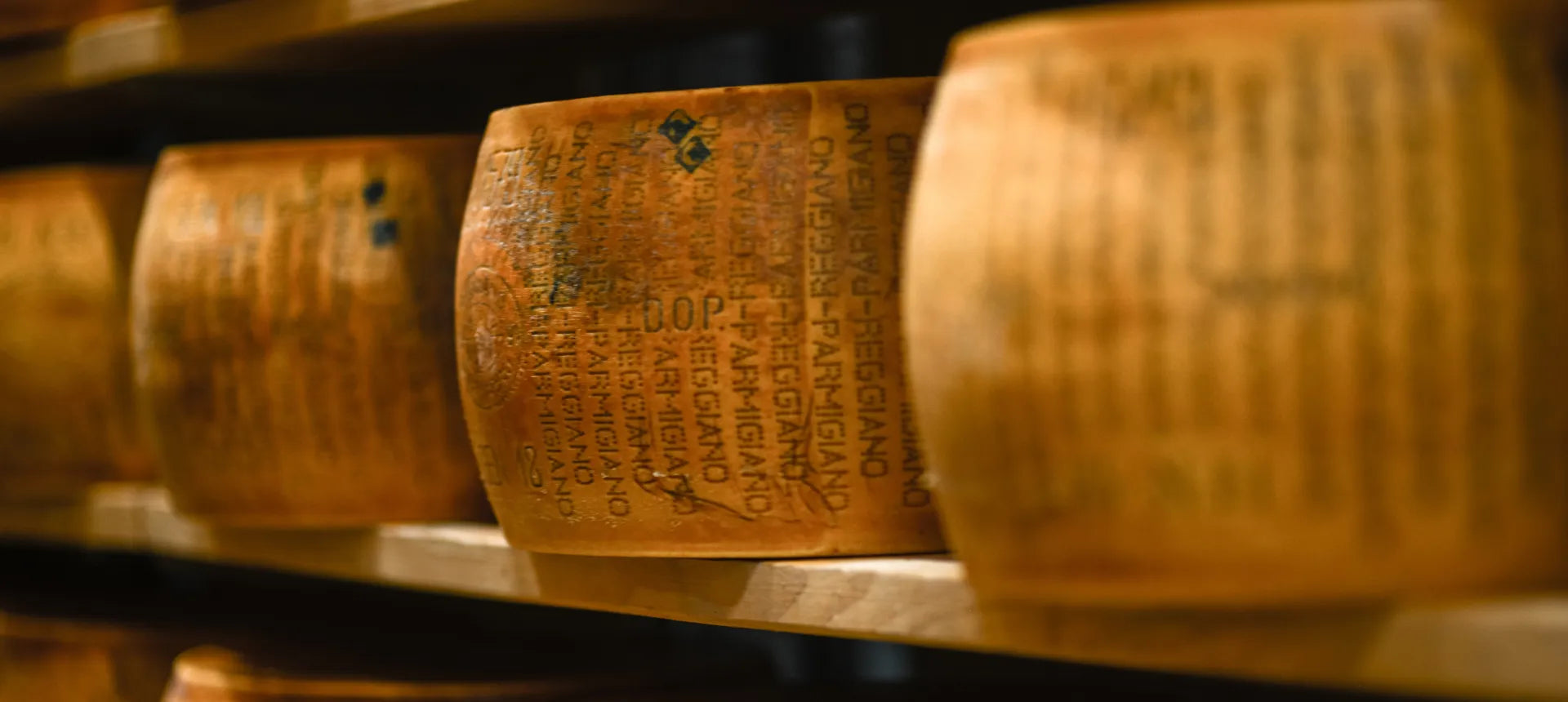 Forme di Parmigiano Reggiano stagionato su scaffali di legno, evocano tradizione e sapore autentico italiano.
