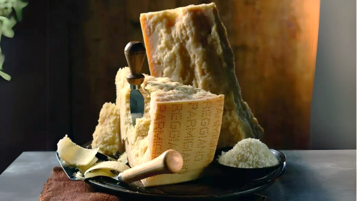 Forma profumata di Parmigiano Reggiano su tagliere rustico, con coltelli da formaggio pronti all'uso.