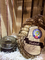 Un culatello stagionato per 12 mesi, elegantemente avvolto in una rete, posa vicino a un vaso di spezie su trucioli di legno, con etichetta 'cavaliere'.