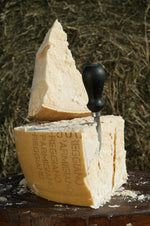 Un pezzo di Parmigiano Reggiano DOP stagionato 24 mesi posato su una tavola rustica, con un coltello da formaggio affondato, evocando i sapori autentici della montagna.