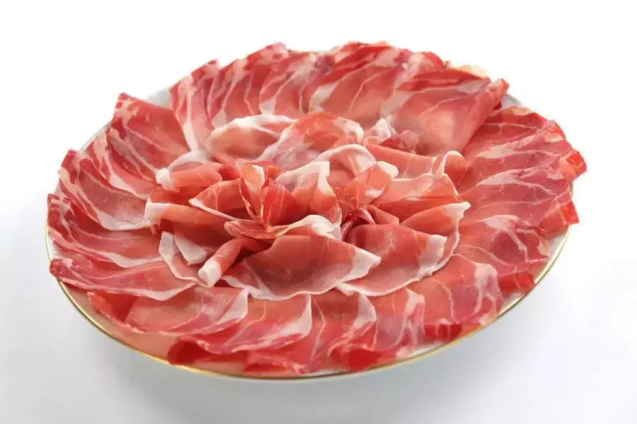 Delizioso affettato di prosciutto stagionato, disposto artisticamente a forma di rosa su un piatto, valorizzando i colori e i sapori autentici dell'Italia.
