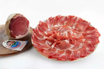 Un fiocco di Prosciutto invecchiato 9 mesi, succoso, con cotenna, presentato sia intero che in fette delicate su un piatto, ideale per aperitivi raffinati.