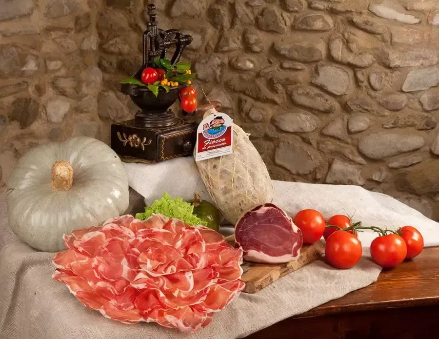 Un invitante fiocco di prosciutto di 9 mesi, sapientemente tagliato a metà e stagionato dolcemente, svela sfumature rosate. È adagiato su un tavolo rustico, accanto a freschi ortaggi, creando un'atmosfera calda e accogliente.