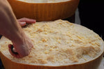 Una mezza forma di Parmigiano Reggiano DOP di 24 mesi, con la sua crosta dorata, è pronta per deliziare i tuoi sensi. Mani esperte la stanno affettando.
