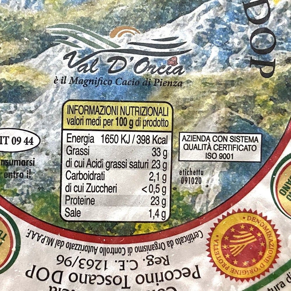 Pecorino Toscano DOP-ost från Val D'Orcia, märkt och certifierad, med 398 kcal och 33 g fett per 100 g, mot en bakgrund av berg.