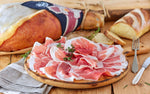Deliziose fette di Prosciutto di Parma DOP, stagionato per 24 mesi, posate su un piatto rustico, accompagnate da pane fresco e fragrante, disposte su un tavolo di legno.