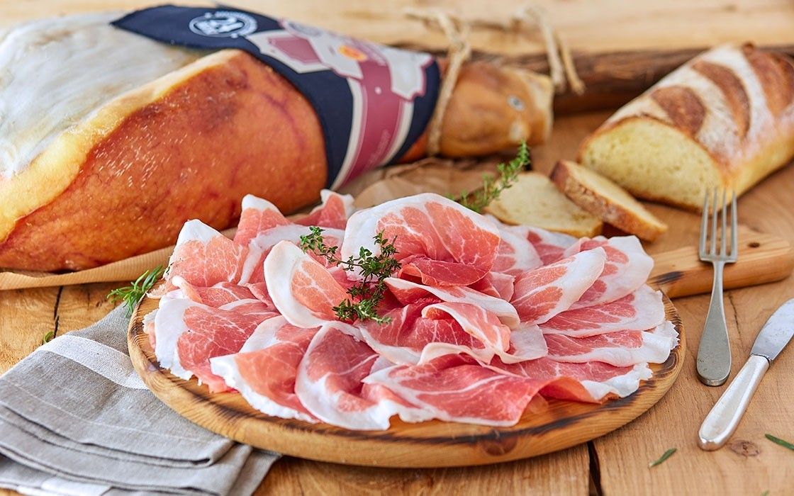 Deliziose fette di Prosciutto di Parma DOP, stagionato per 24 mesi, posate su un piatto rustico, accompagnate da pane fresco e fragrante, disposte su un tavolo di legno.