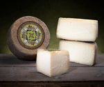Un intero formaggio Pecorino biologico stagionato in grotta, con alcune fette affianco, posato su un tavolo rustico. Lo sfondo è scuro, per un effetto suggestivo.