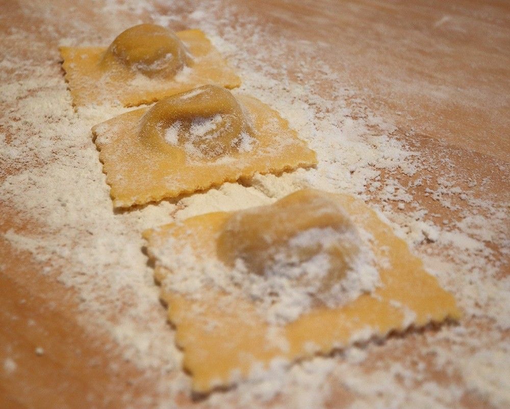 Squisiti tortelli artigianali di zucca presentati su un tavolo infarinato, con l'esterno di pasta all'uovo dorata che avvolge un ripieno tradizionale e saporito.