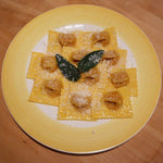 Un piatto giallo brillante ospita deliziosi tortelli artigianali di zucca, di un colore dorato, arricchiti da salvia e parmigiano grattugiato.