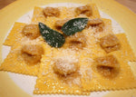 Squisiti tortelli artigianali ripieni di zucca, presentati su un piatto bianco, arricchiti da foglie di salvia e cosparso di parmigiano abbondante.