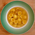 Deliziosi anolini fatti a mano, conditi con Parmigiano Reggiano DOP e serviti in brodo caldo su un piatto verde, pronti per essere gustati.
