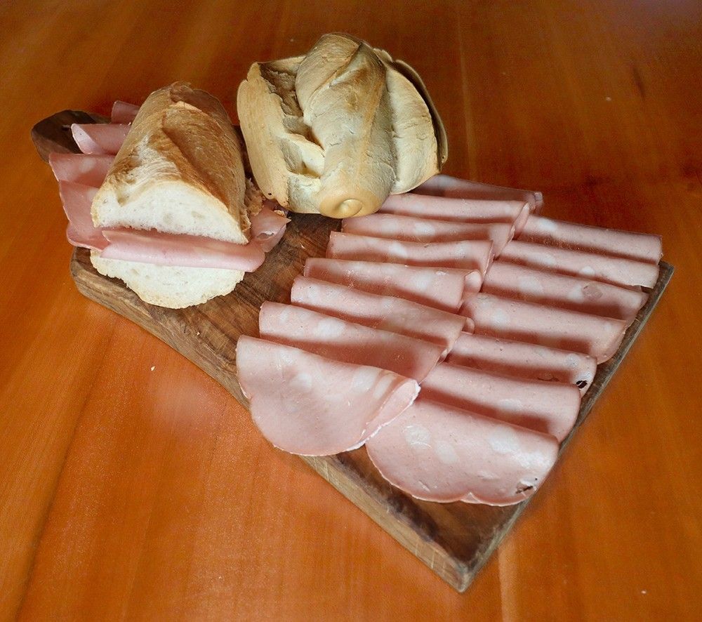 Un invitante panino con fette di autentica Mortadella di Bologna IGP, servito su un rustico tagliere in legno per uno spuntino all'italiana.