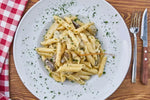 Un appetitoso piatto di pasta cremosa impreziosito da funghi porcini secchi, pronto per deliziare il palato, si presenta su un tavolo rustico con una decorazione di prezzemolo.