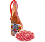 Metà di un Prosciutto di Parma DOP, disossato e in rete rossa, stagionato per 16 mesi. Le sue fette rosa delicate, servite su un piatto bianco, rivelano un sapore dolce e un aroma intenso.