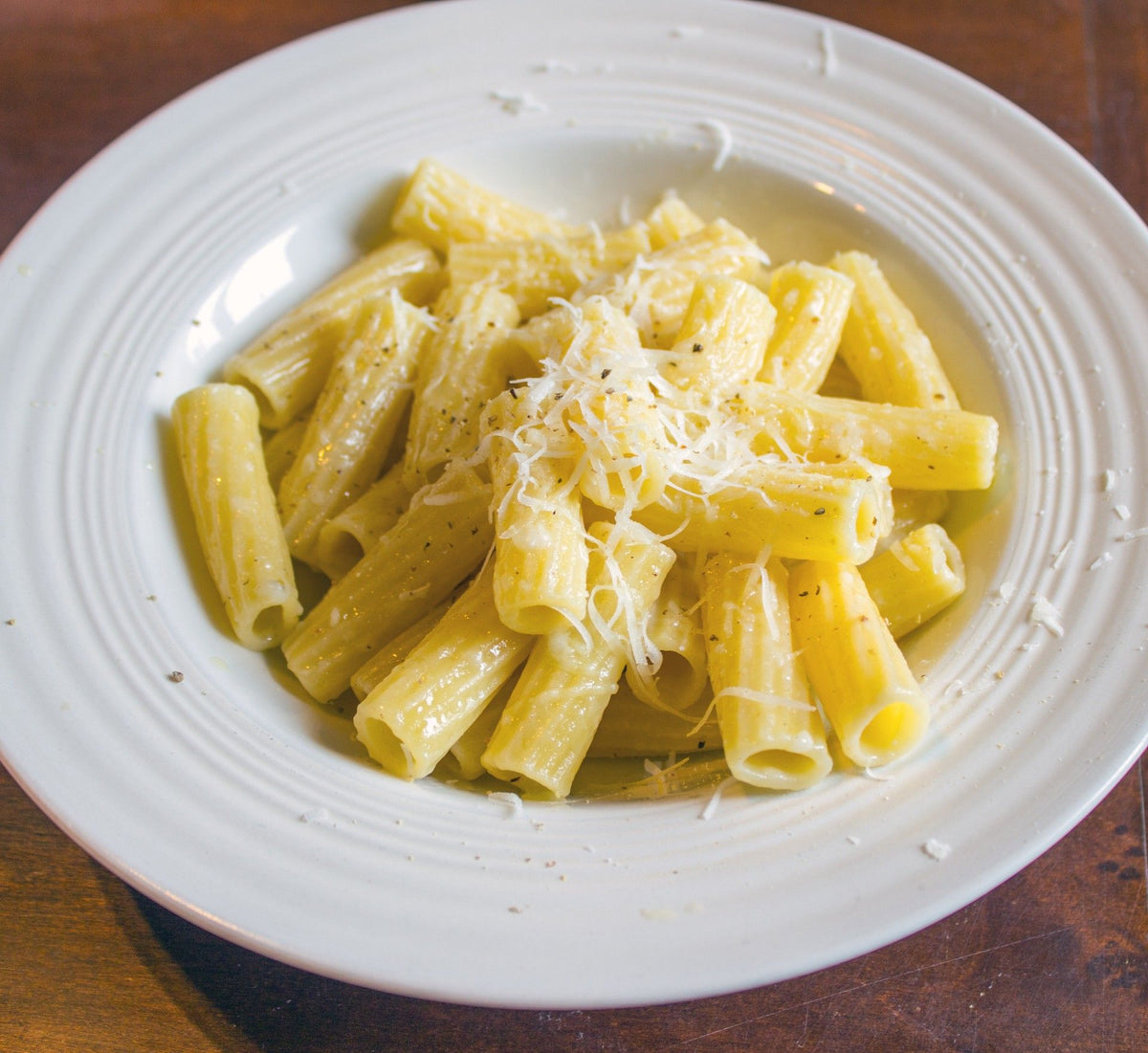 En elegant hvit tallerken med al dente tortiglioni, deilig tilberedt med smeltet smør og revet parmesanost.