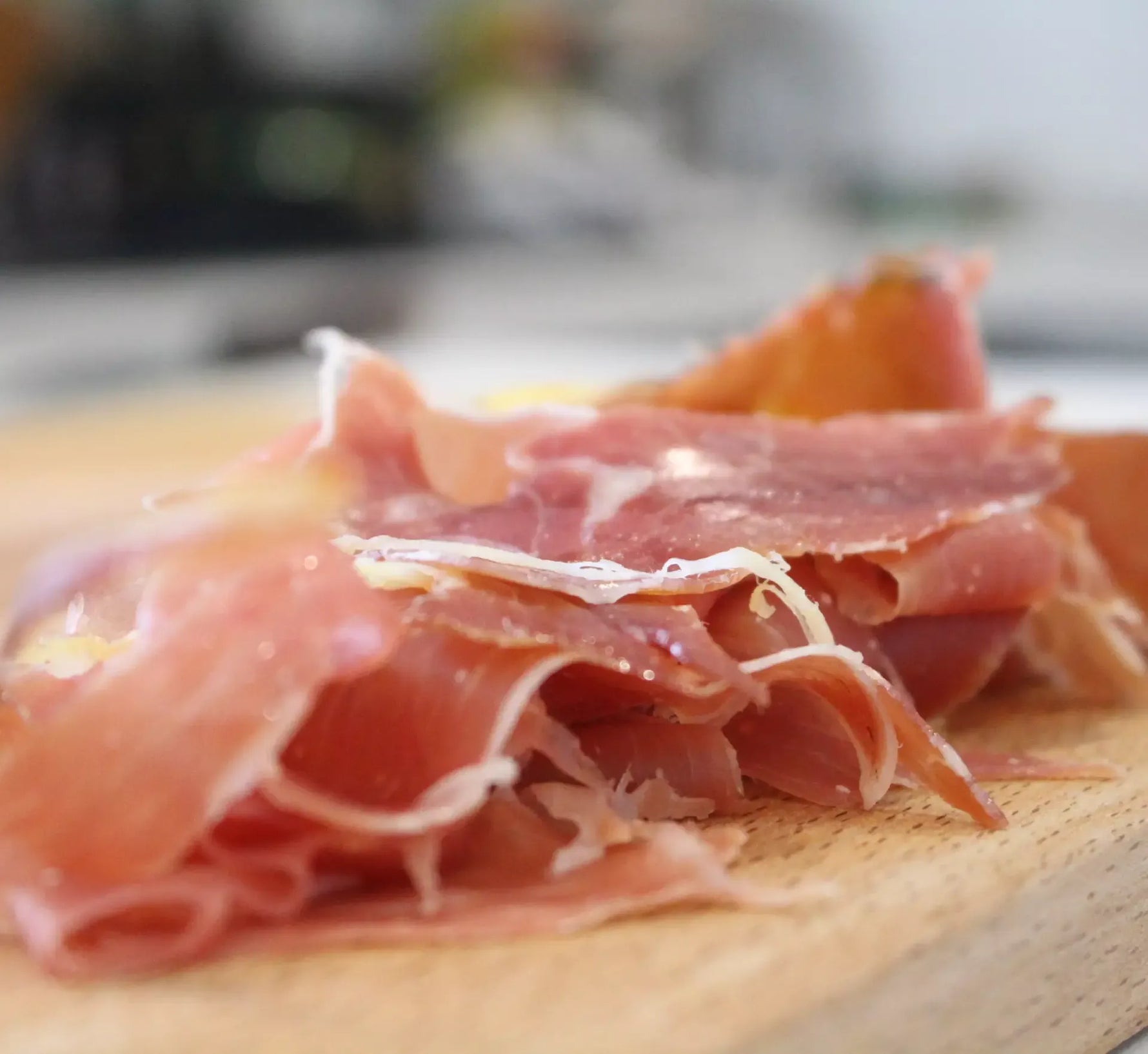 Delicate fette di Prosciutto di Parma DOP, stagionato per 16 mesi e disossato, posate su un tagliere in legno per un sapore genuino.
