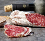 Un salame di Felino IGP, con la sua caratteristica venatura marmorizzata, posato su un tavolo rustico accanto a un vino rosso invitante.