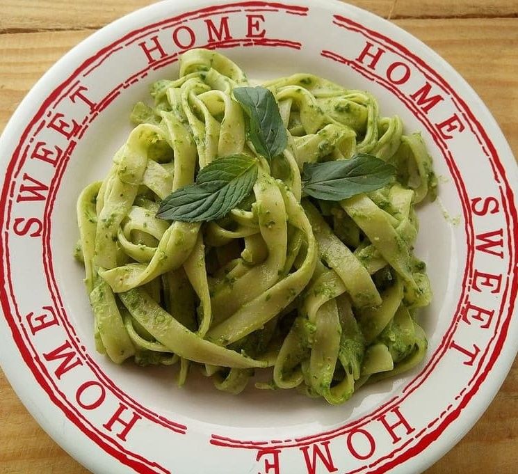 Deilige økologiske pappardelle med egg, tilberedt med grønn pesto og beriket med basilikumblader, servert på en tallerken med påskriften «Home Sweet Home».