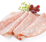 Una Mortadella di Bologna IGP, caratterizzata da fette rosee e cremose e arricchita da pistacchi, elegantemente disposta su un tagliere, accompagnata da uva e foglie verdi come decorazione.