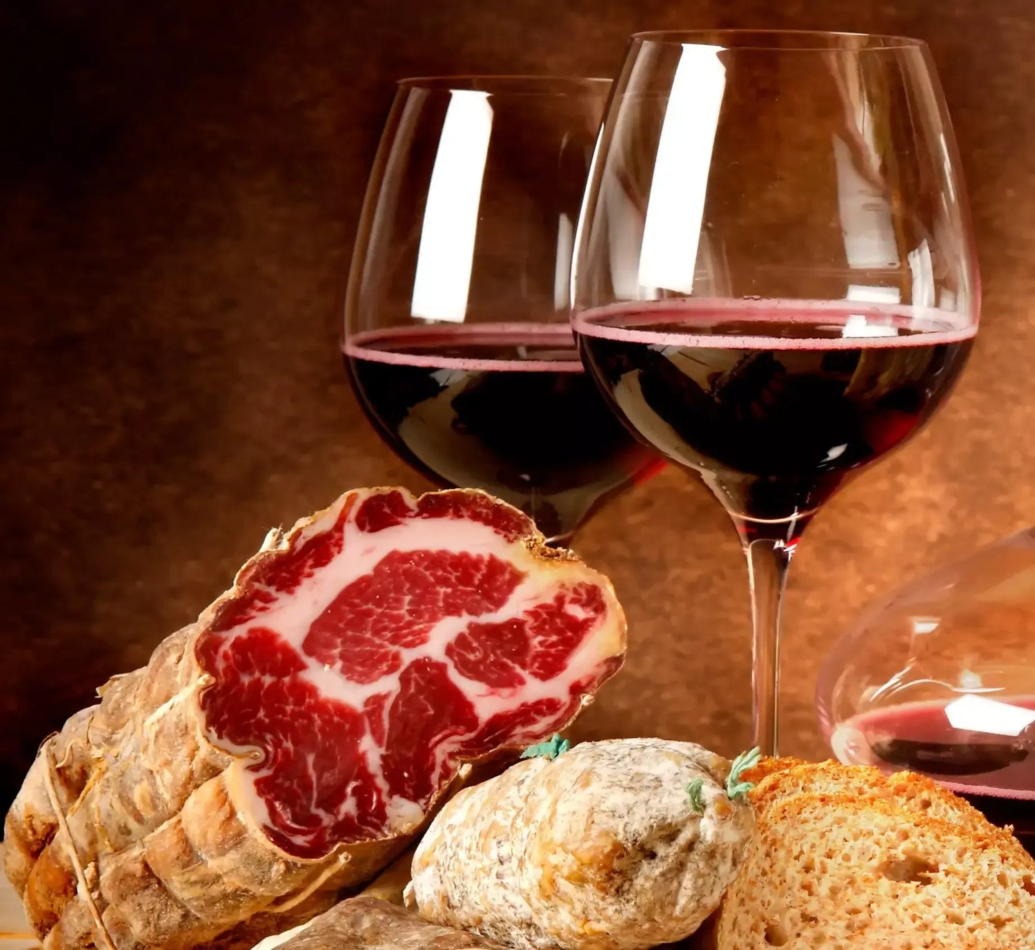 Su una tavola rustica, una Coppa di Parma IGP stagionata è affettata con eleganza, accompagnata da calici di vino rosso.