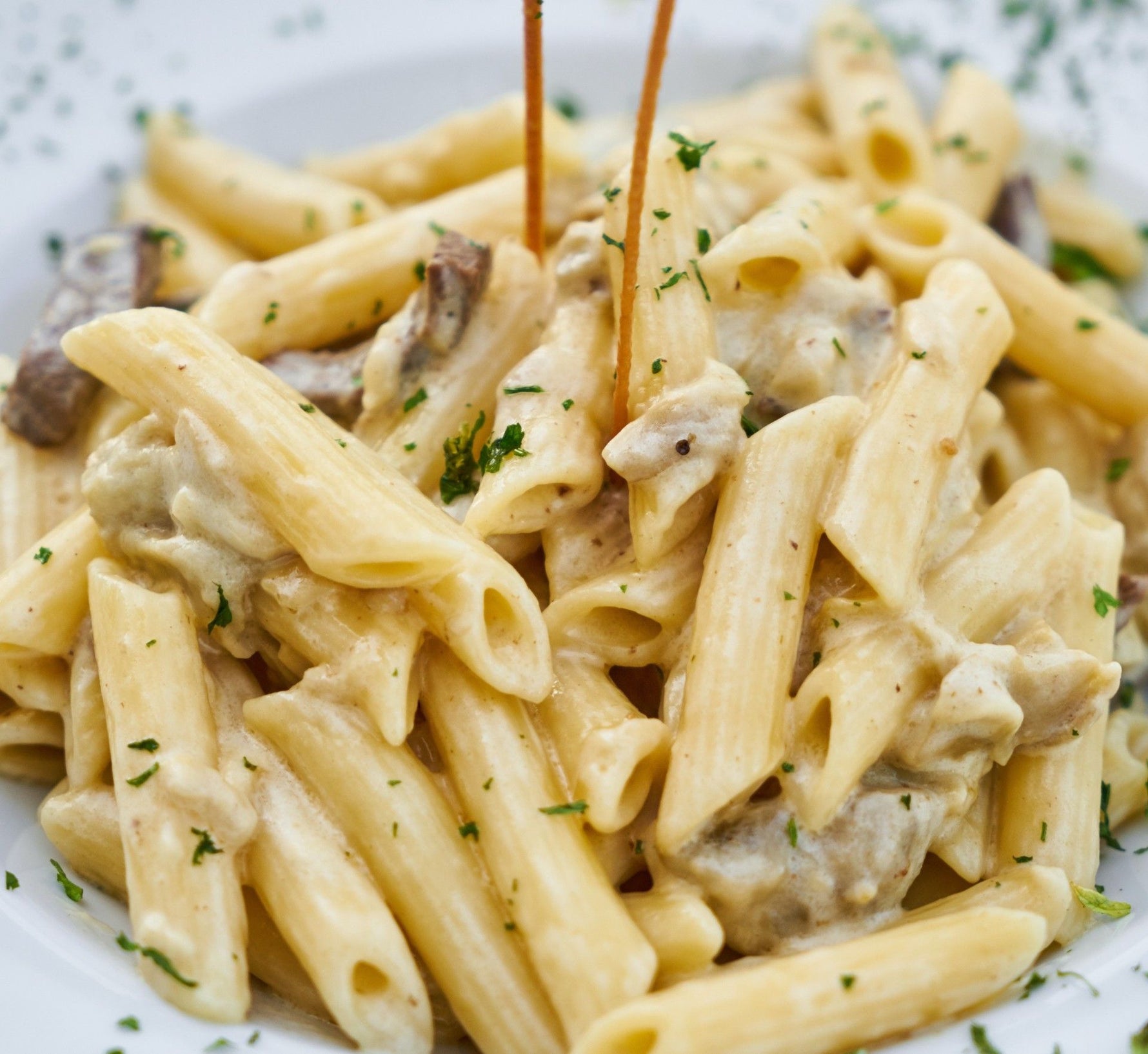 Una porzione di penne rigate biologiche, immerse in una salsa cremosa di formaggio e funghi, impreziosite da prezzemolo fresco.