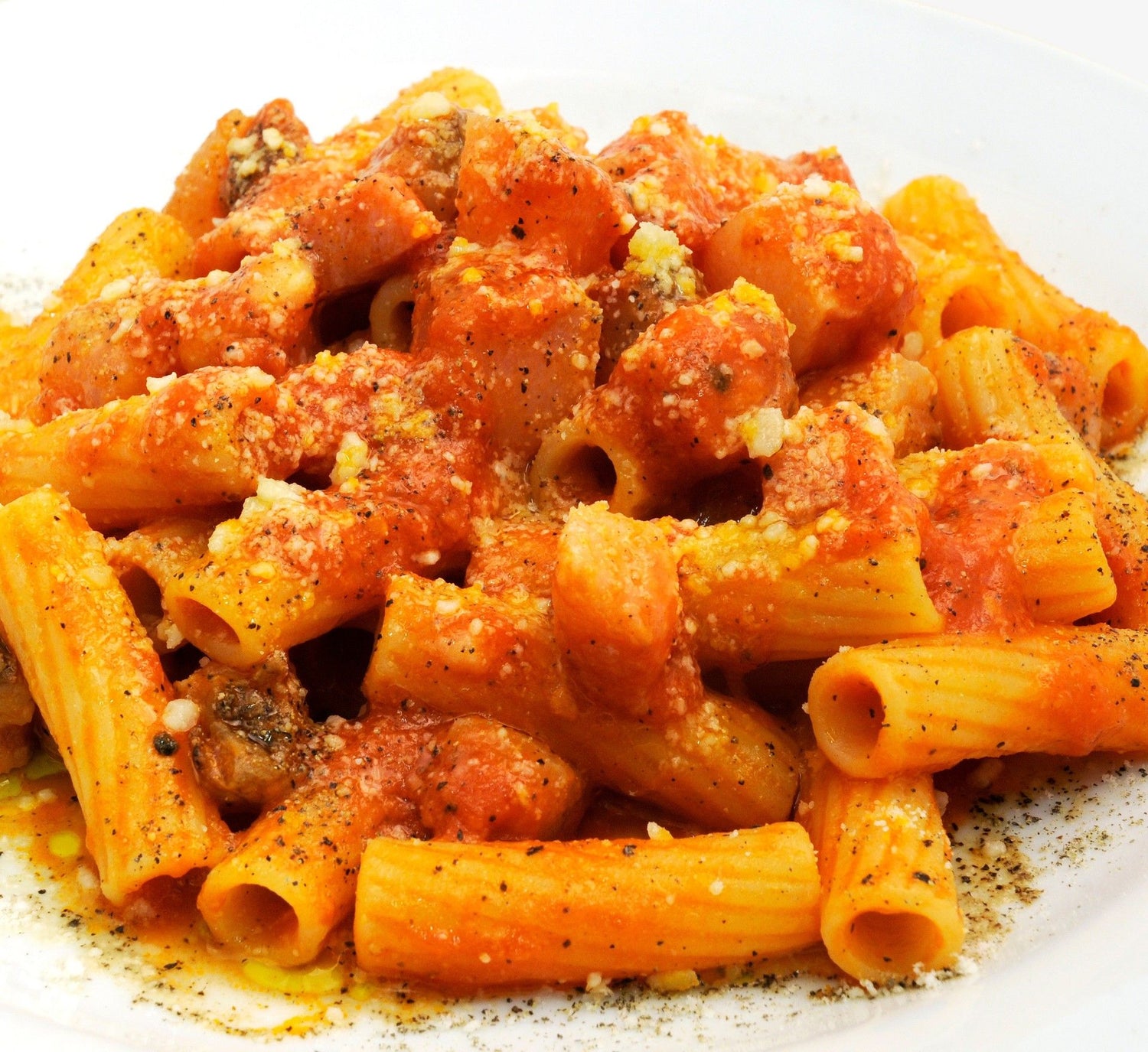 Un piatto bianco ospita deliziosi tortiglioni, ricoperti di un sugo di pomodoro succoso, arricchito da pepe nero e formaggio grattugiato.