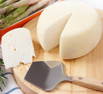 Una fetta di Pecorino Toscano DOP è posta su un tagliere di legno, accanto a un coltello e asparagi freschi.