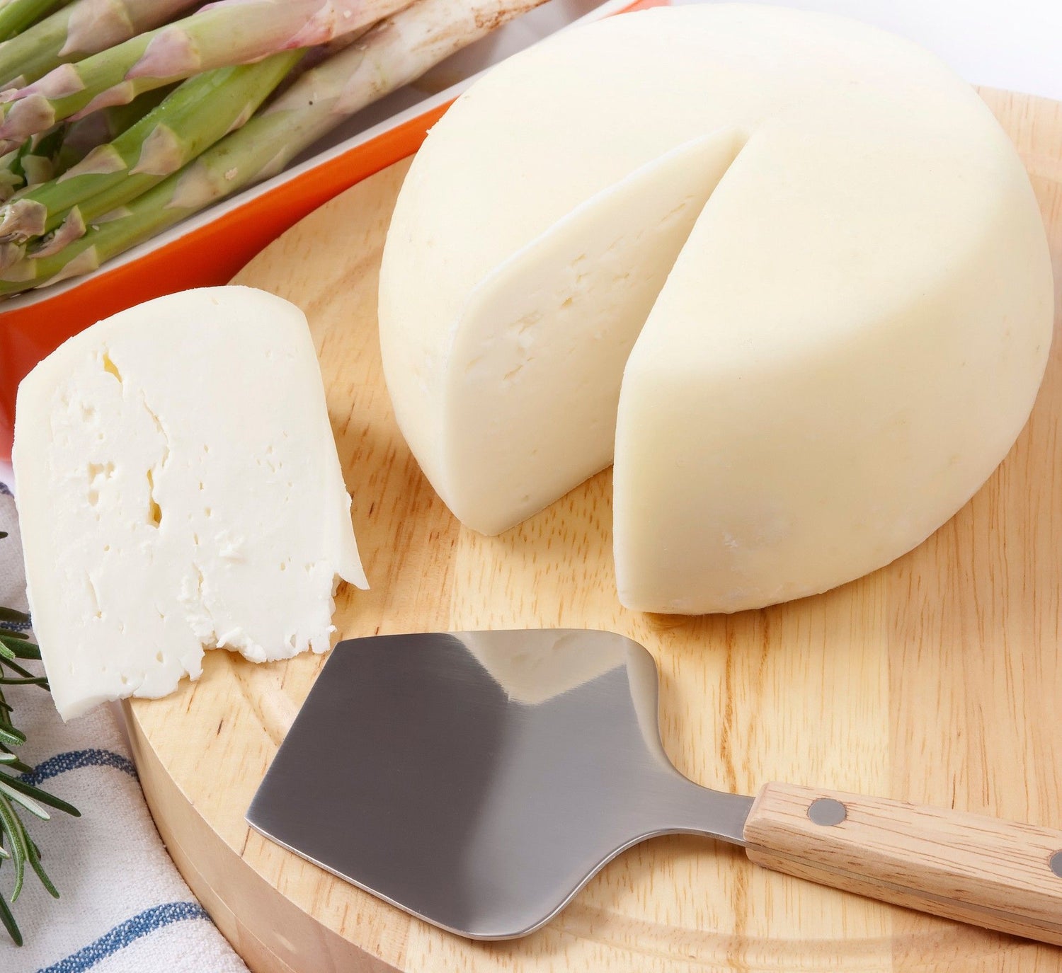 Una fetta di Pecorino Toscano DOP è posta su un tagliere di legno, accanto a un coltello e asparagi freschi.