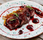 Una gustosa carne succosa impreziosita da salsa biologica di ciliegie e zenzero, accompagnata da verdure grigliate e rosmarino fresco, servita su un piatto rustico.