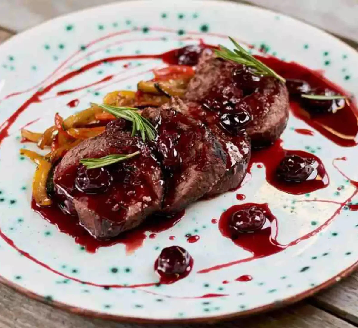 Una gustosa carne succosa impreziosita da salsa biologica di ciliegie e zenzero, accompagnata da verdure grigliate e rosmarino fresco, servita su un piatto rustico.