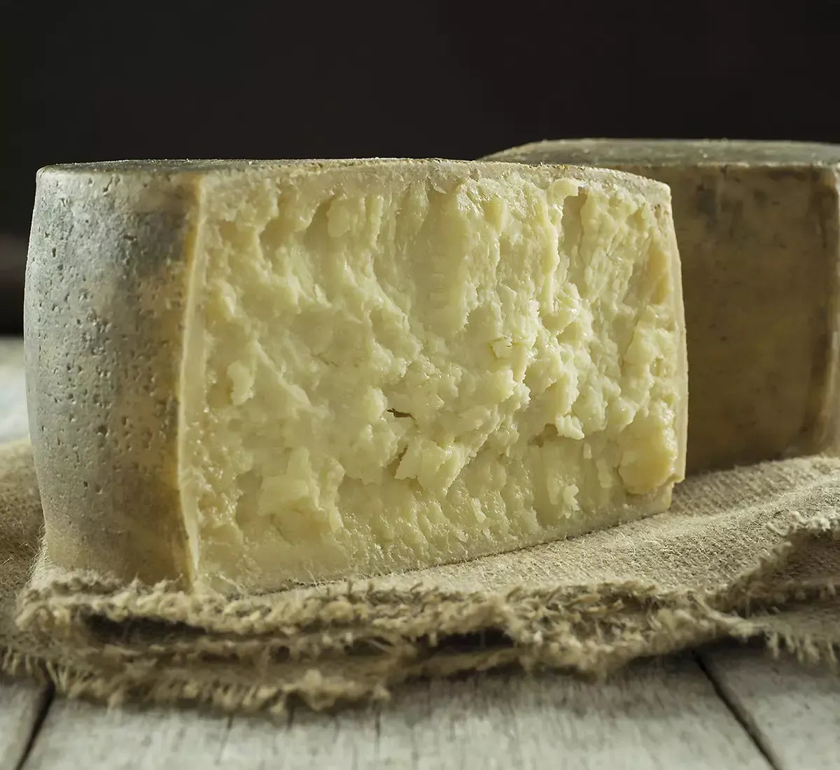 Un gustoso formaggio pecorino stagionato di Amatrice si presenta con la sua crosta rustica e pasta interna friabile, posato su una tela grezza.