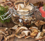Un barattolo di porcini secchi posa su un tavolo rustico, accompagnato da pigne. Ideale per piatti gourmet che valorizzano i gusti autunnali.