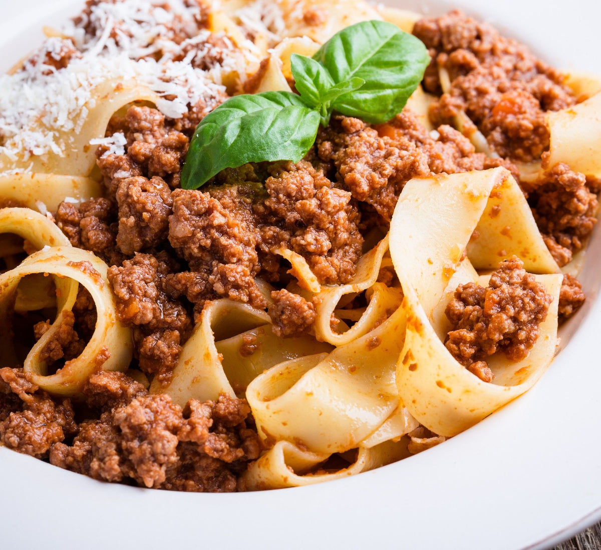 Fristende økologiske pappardelle med egg, tilberedt med en smakfull kjøttragù, beriket med parmesanflak og fersk basilikum.