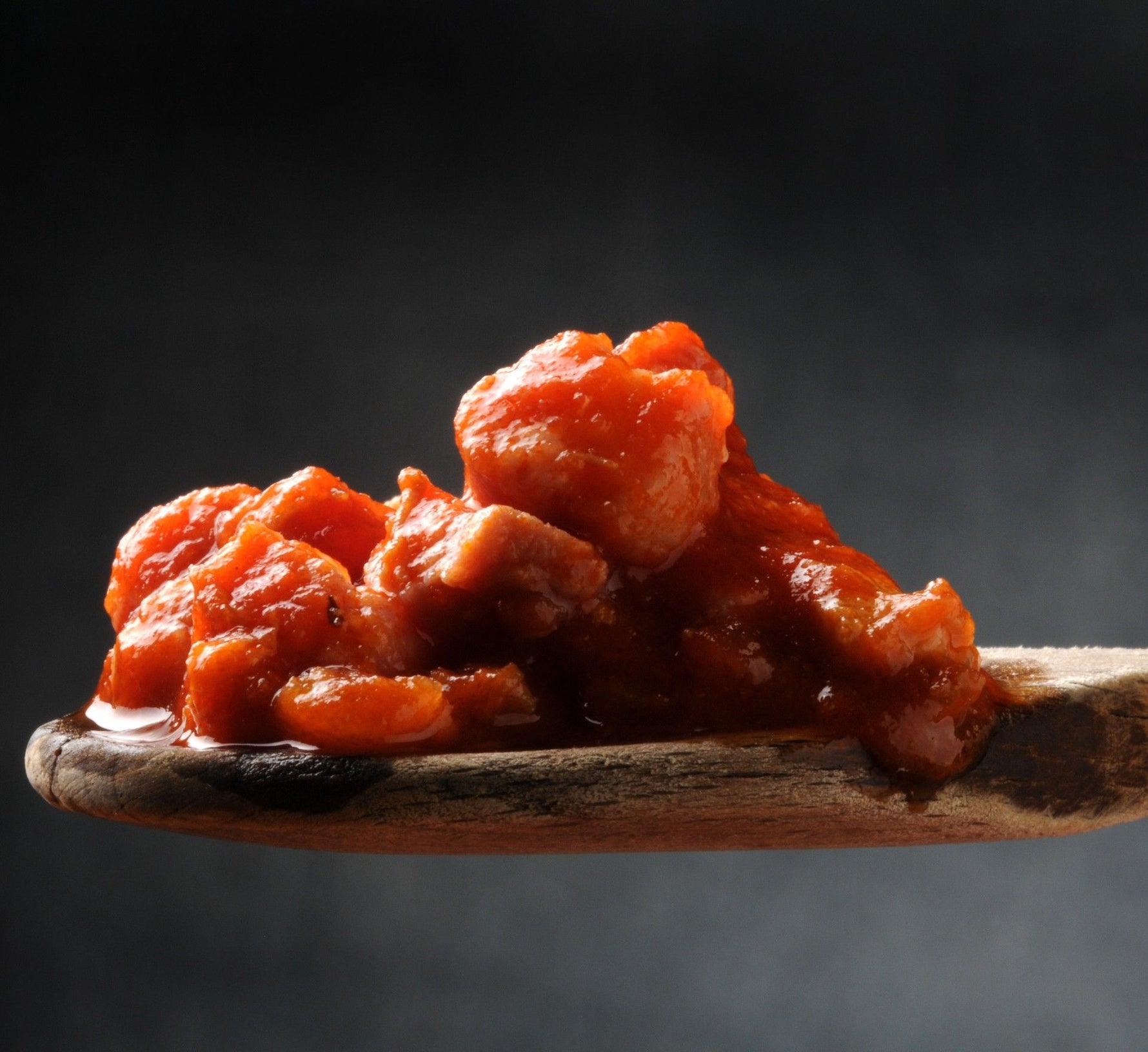 Un cucchiaio di legno contiene la salsa Ortolina Classica, mostrando una ricca texture rossa, un profumo intenso di pomodoro e spezie, pronta per essere gustata.
