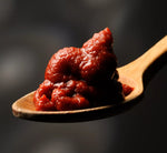 Sullo sfondo, un cucchiaio di legno regge l'Ortolina Piccante, salsa cremosa dal rosso intenso, che sprigiona un aroma speziato.