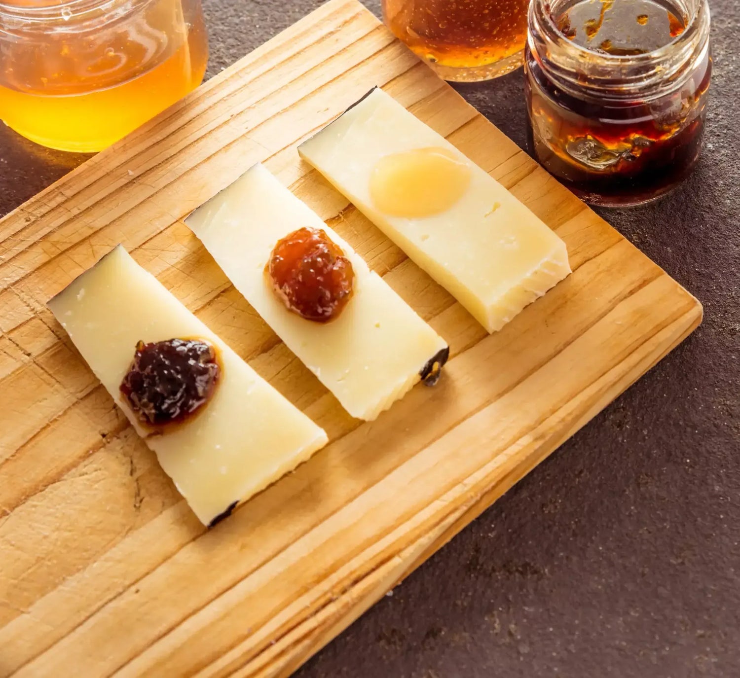 Una mezza forma di Pecorino Biologico stagionato in grotta, presentata su un tagliere rustico con miele e confettura per assaggio.