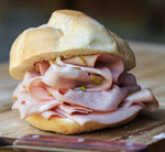 Un panino invitante con fette di mortadella rosa, arricchito da tocchi di pistacchi, poggia su un tagliere in legno.