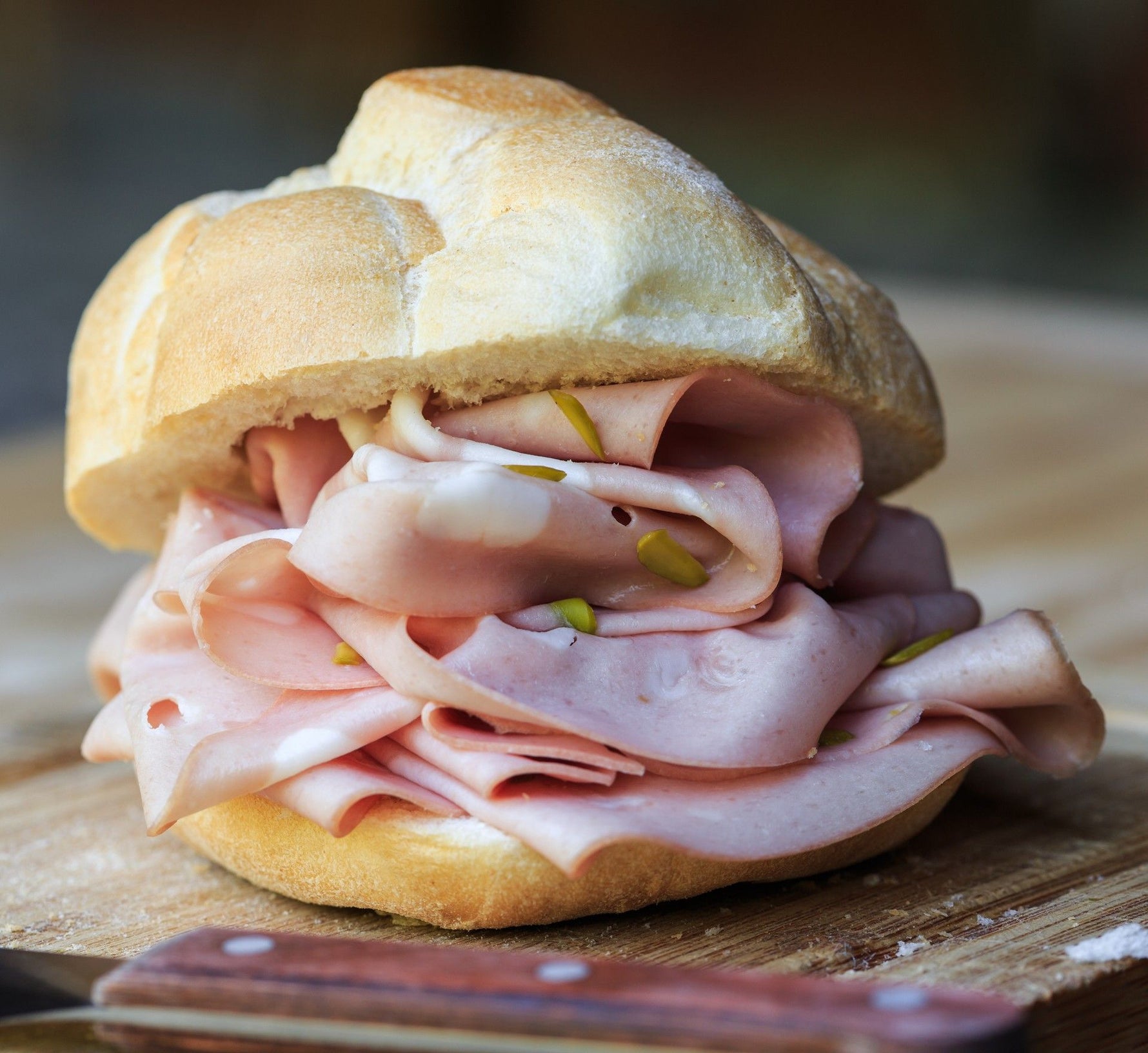 Un panino invitante con fette di mortadella rosa, arricchito da tocchi di pistacchi, poggia su un tagliere in legno.