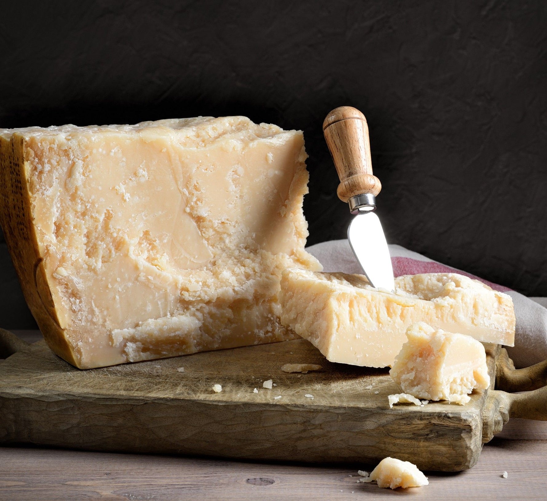 Un formaggio stagionato affettato è presentato su un tagliere di legno, con un coltello a fianco, esibendo la sua rusticità e texture, ideale per i gourmet.