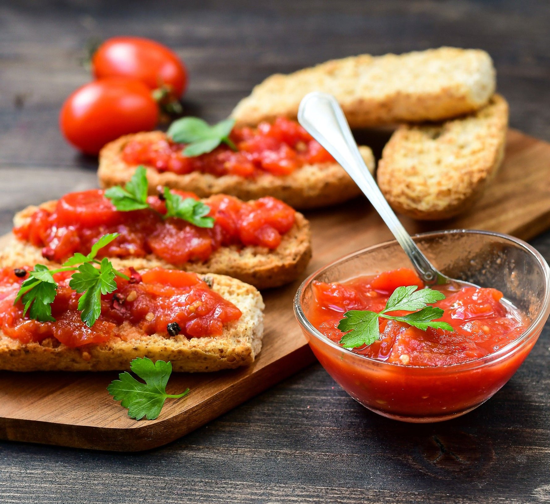 Un'autentica delizia italiana: salsa per bruschetta su pane croccante, arricchita da prezzemolo fresco, con pomodori succosi sullo sfondo.