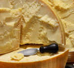 Una forma intera di Parmigiano Reggiano DOP Vacche Rosse, stagionata per 24 mesi, con la sua crosta dorata e un coltello affianco, pronta per essere gustata.