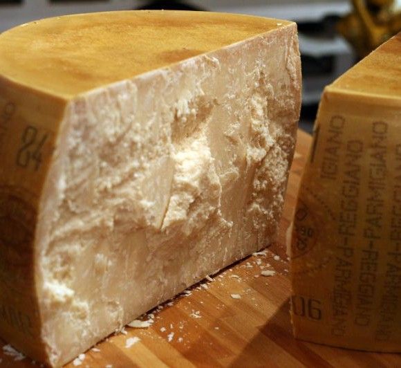 Un formaggio Parmigiano Reggiano DOP di montagna, stagionato per 24 mesi, posato su un tagliere di legno con coltello affianco, dal sapore intenso e consistenza friabile.