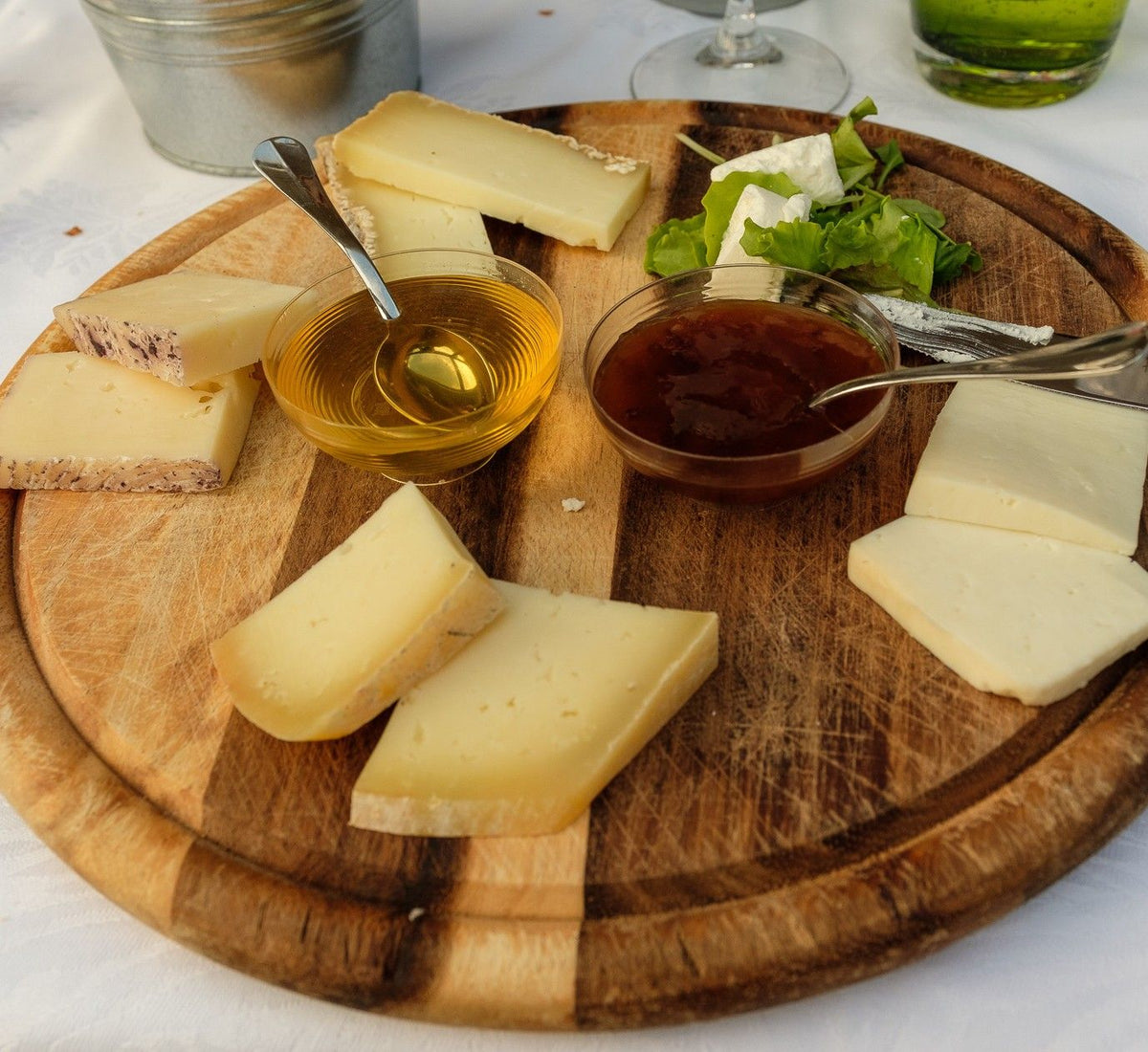 Una porzione di Pecorino Toscano stagionato, disposto su un tagliere in legno, circondato da miele, marmellata e verdure fresche.