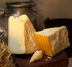 Un biologico Parmigiano Reggiano DOP, stagionato 24 mesi, delle Vacche Rosse, posato su un tagliere rustico con una fattoria come sfondo.