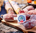 Squisite fette di salame artigianale Cavalier Umberto Boschi, posate su un tagliere rustico, immerse in un ambiente naturale e accogliente.